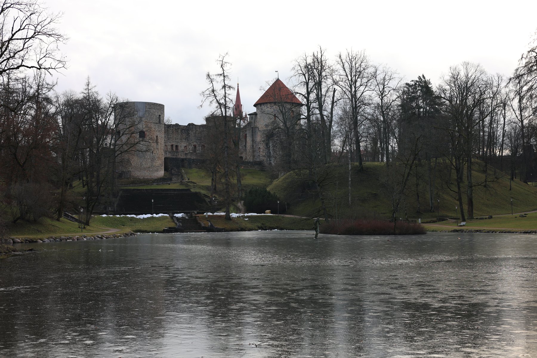 Le château de Cēsis se reflétant dans un étang d&rsquo;hiver entre des arbres dénudés