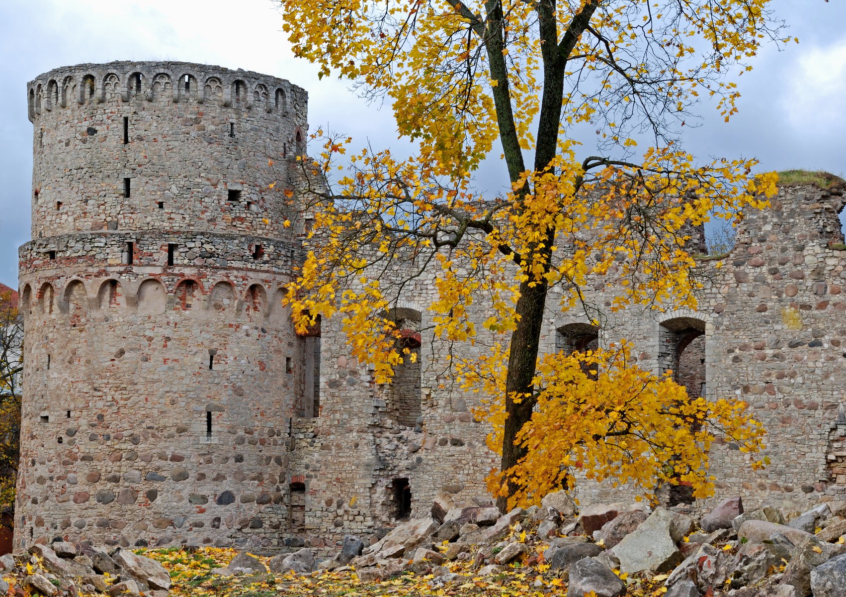 Les murs en pierre du château de Cēsis encadrés par des feuilles d&rsquo;automne dorées
